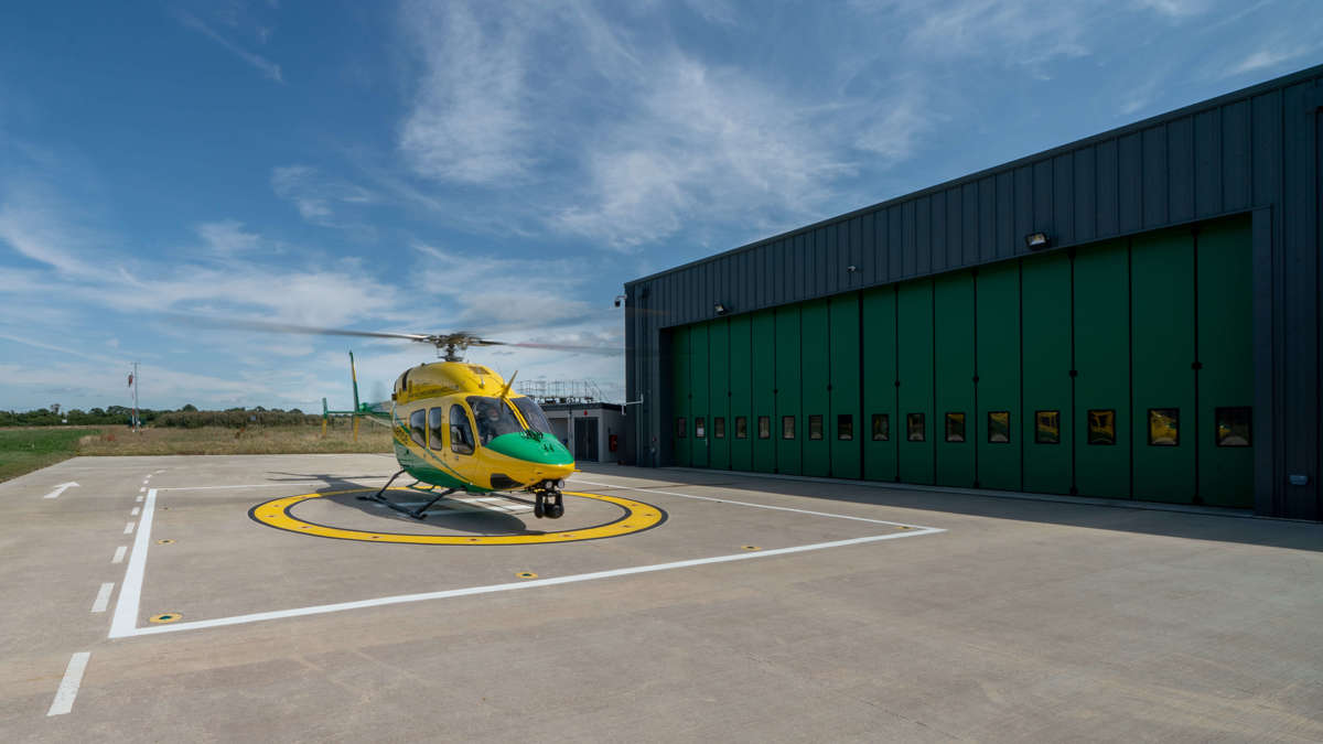 The yellow and green helicopter landed on the helipad against a blue sky with the rotor blades turning.