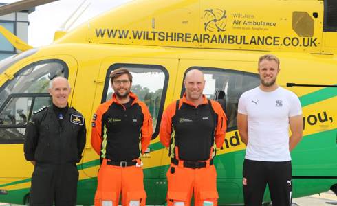 Wiltshire Air Ambulance paramedics and pilot with Swindon Town goalie Lewis in front of Wiltshire Air Ambulance's yellow and green helicopter