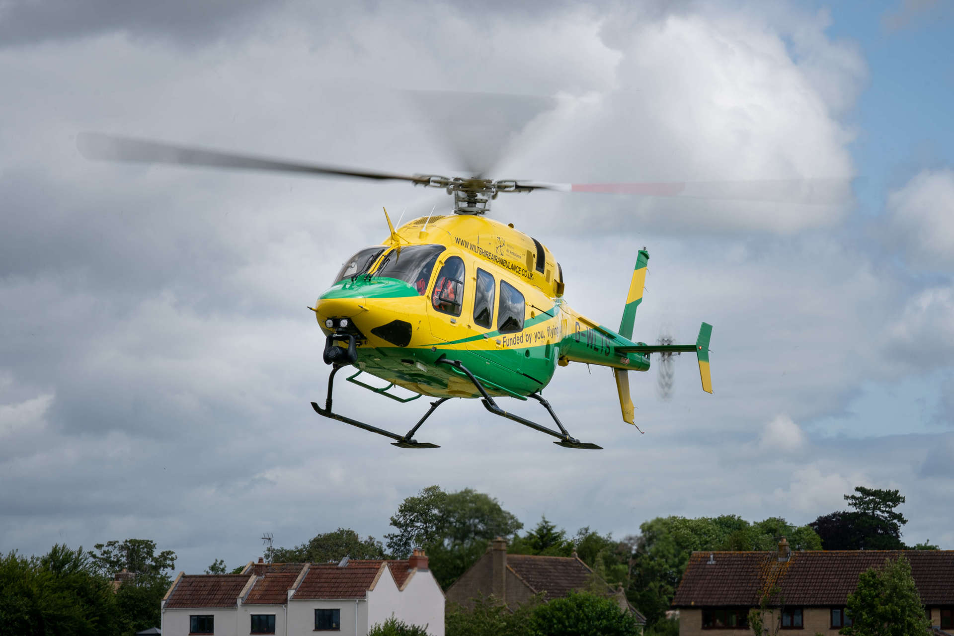 A yellow and green Bell-429 helicopter coming in to land in a field.