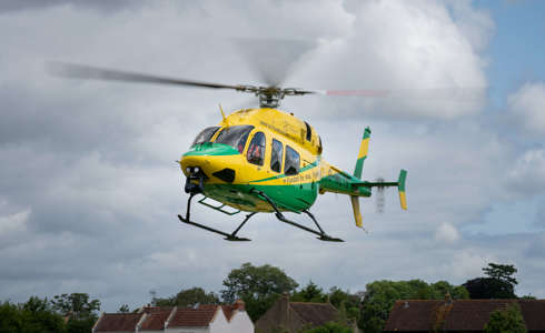 A yellow and green Bell-429 helicopter coming in to land in a field.