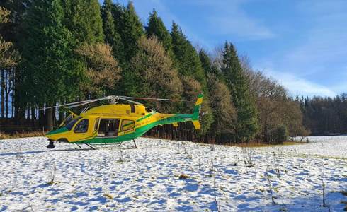 A photograph of the yellow and green helicopter landed in a snowy field with trees in the background.