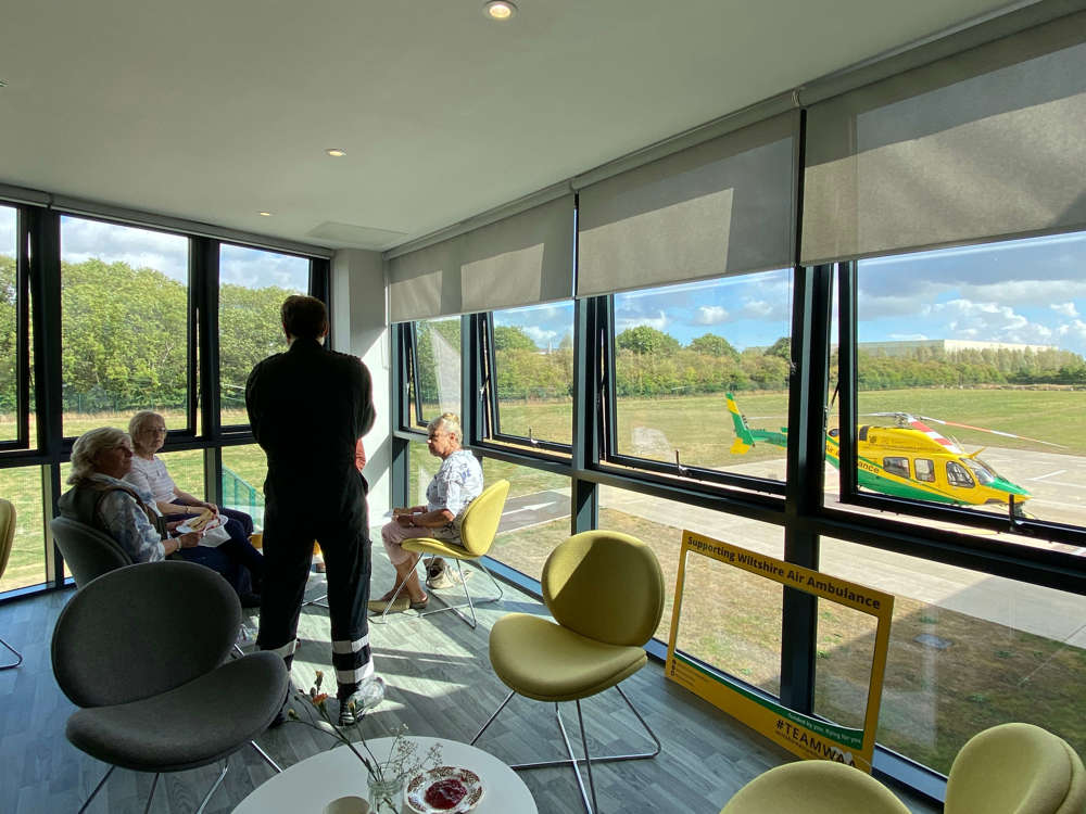 Pilot talking to 3 supporters in a room overlooking the Wiltshire Air Ambulance helicopter and helipad