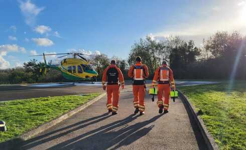 Three paramedics walking towards the helicopter which has landed on a hospital helipad.