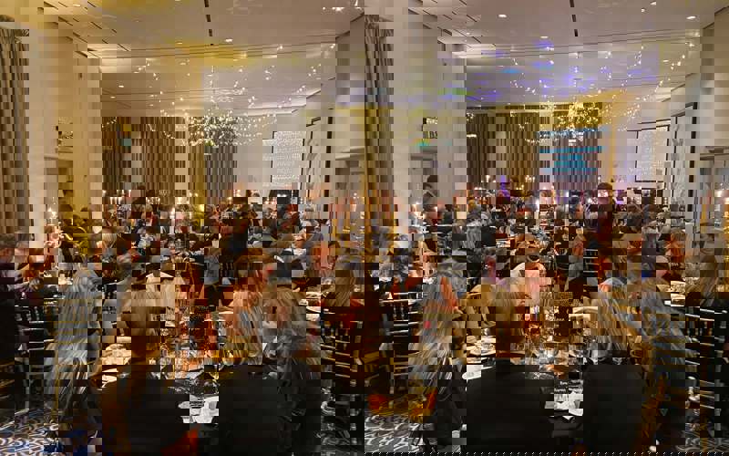 Black and gold themed charity ball. Groups of people wearing smart clothing, sitting on gold chairs around round tables Black and gold themed charity ball. Groups of people wearing smart clothing, sitting on gold chairs around round tables