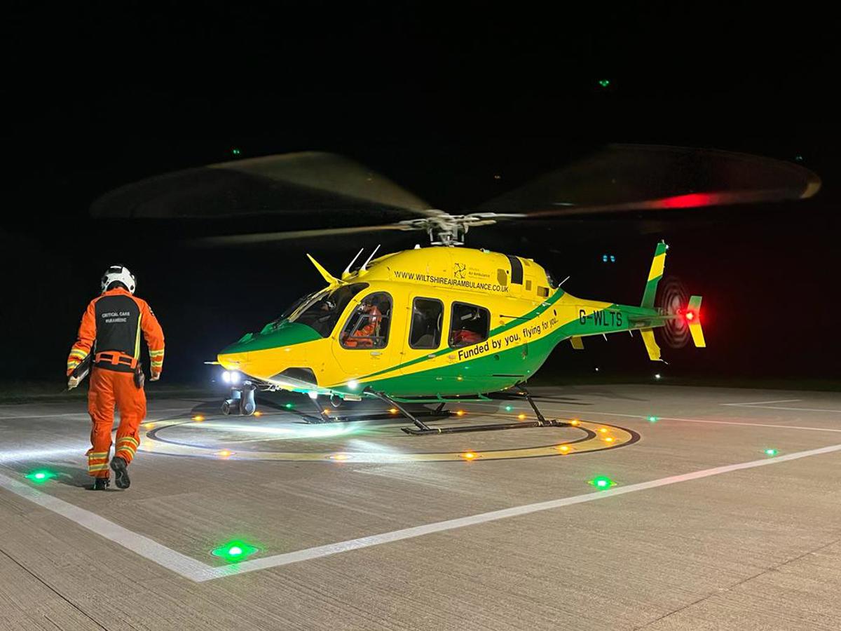 A paramedic wearing an orange flight suit walking towards a yellow and green helicopter A paramedic wearing an orange flight suit walking towards a yellow and green helicopter