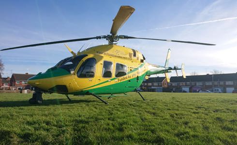 A yellow and green helicopter landed on a green in Swindon, with houses behind