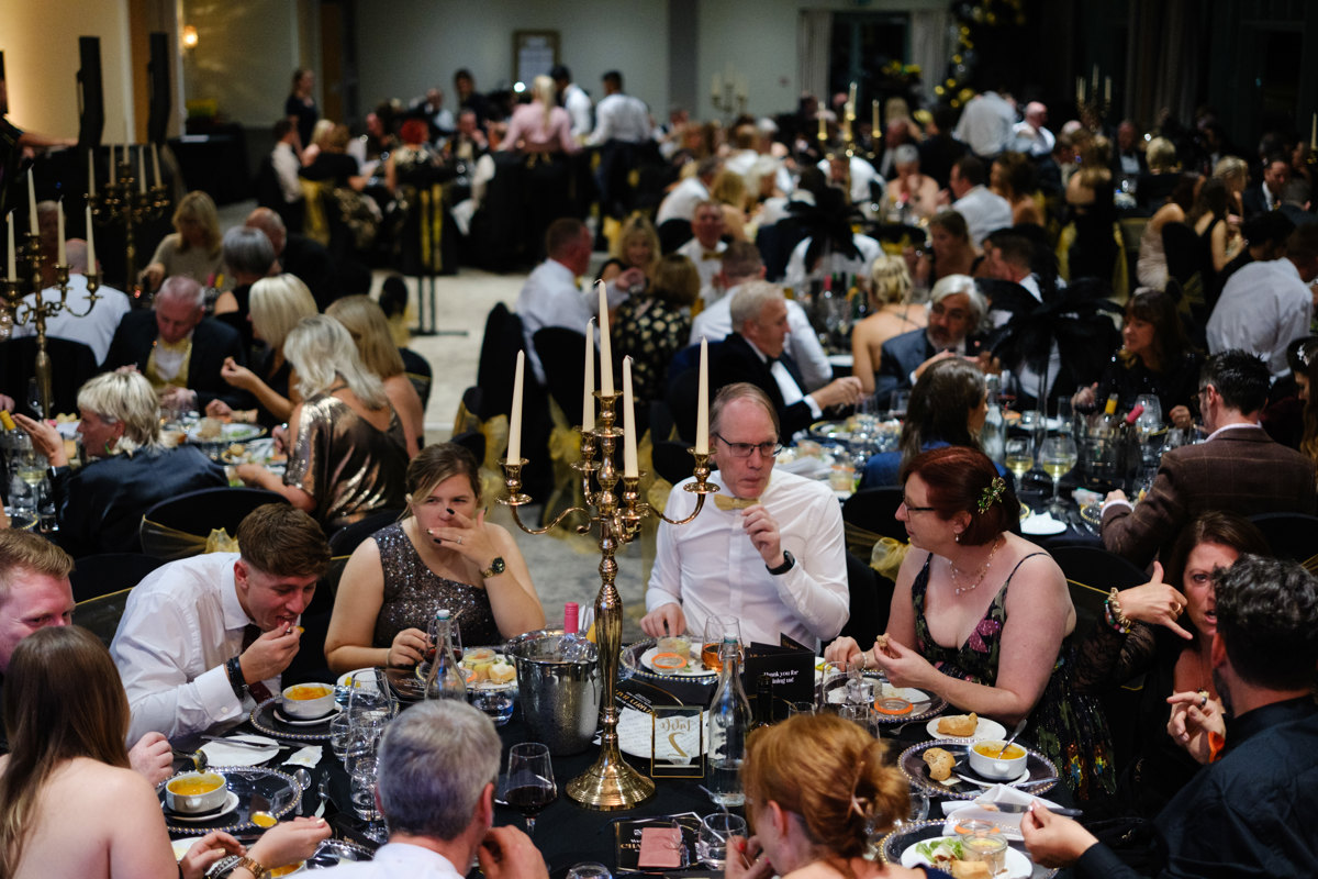 A group of people sitting around tables wearing black and gold A group of people sitting around tables wearing black and gold