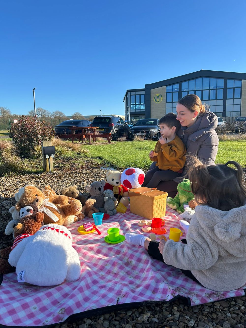 Young children sat with a parent on a picnic blanket with toys, overlooking an airbase