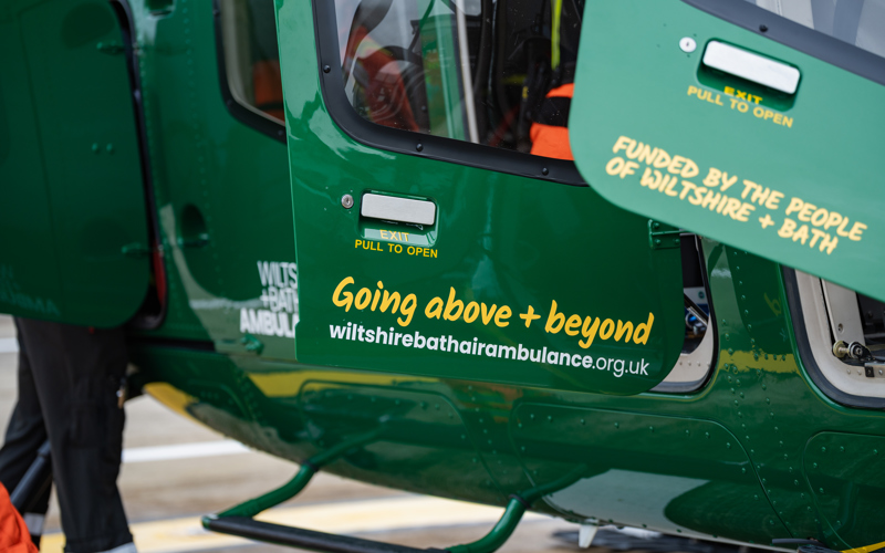 Yellow text with going above + beyond and funded by the people of wiltshire + bath on the doors of a green helicopter