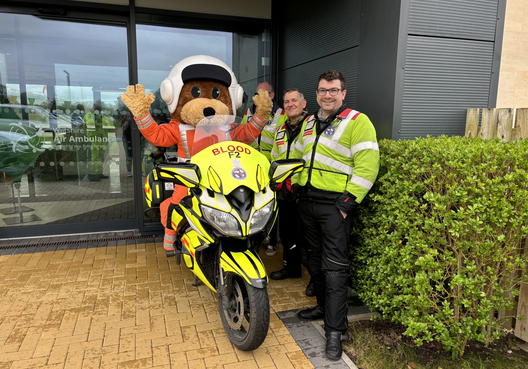 A paramedic bear mascot on a blood bike, with three other blood bikers posing A paramedic bear mascot on a blood bike, with three other blood bikers posing