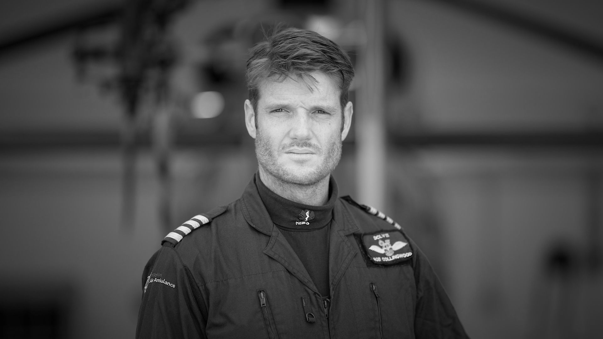 A black and white photograph of a pilot stood in front of the helicopter wearing a flight suit. A black and white photograph of a pilot stood in front of the helicopter wearing a flight suit.