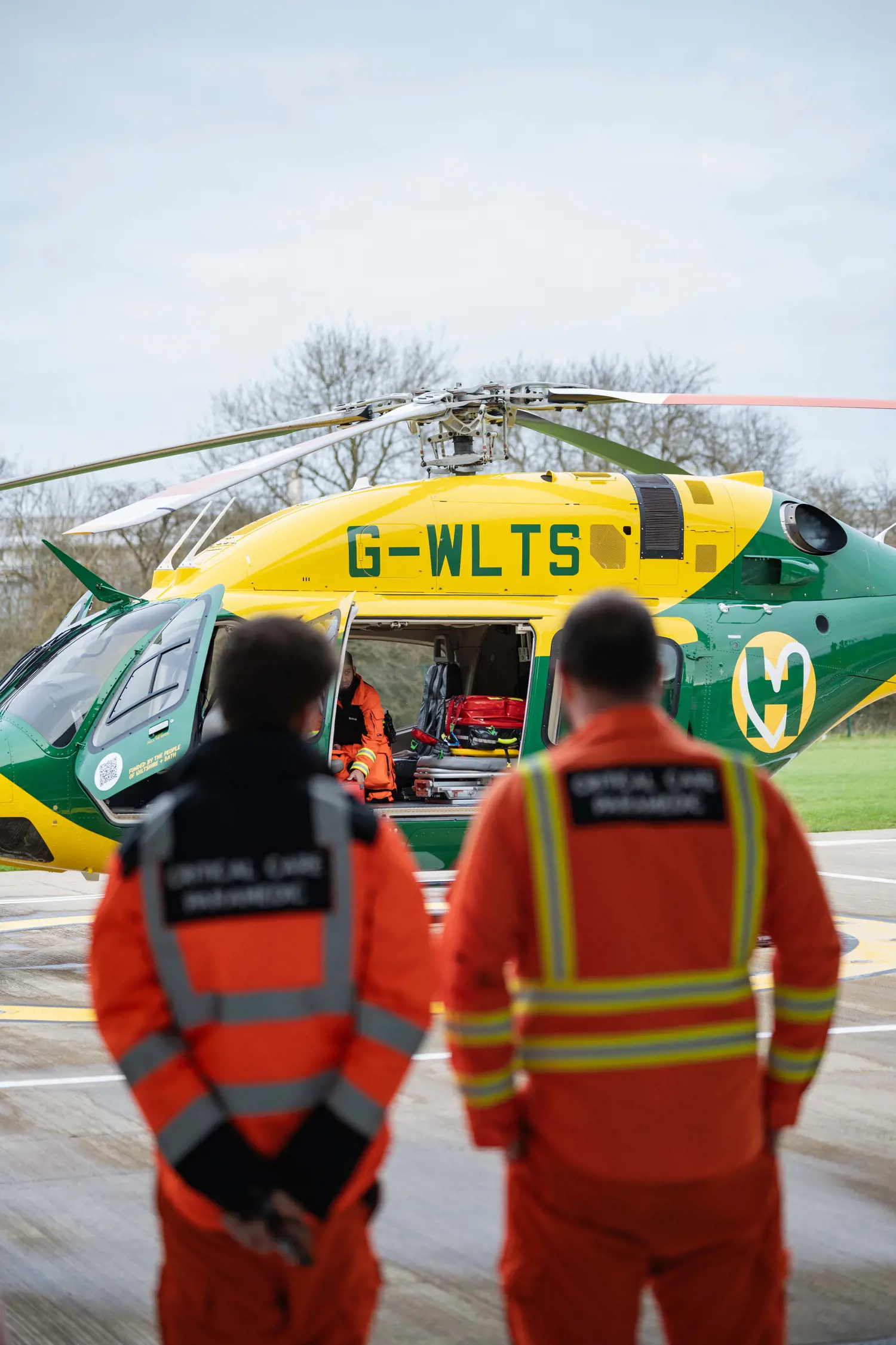 The back of orange jackets, with a yellow and green helicopter in the background